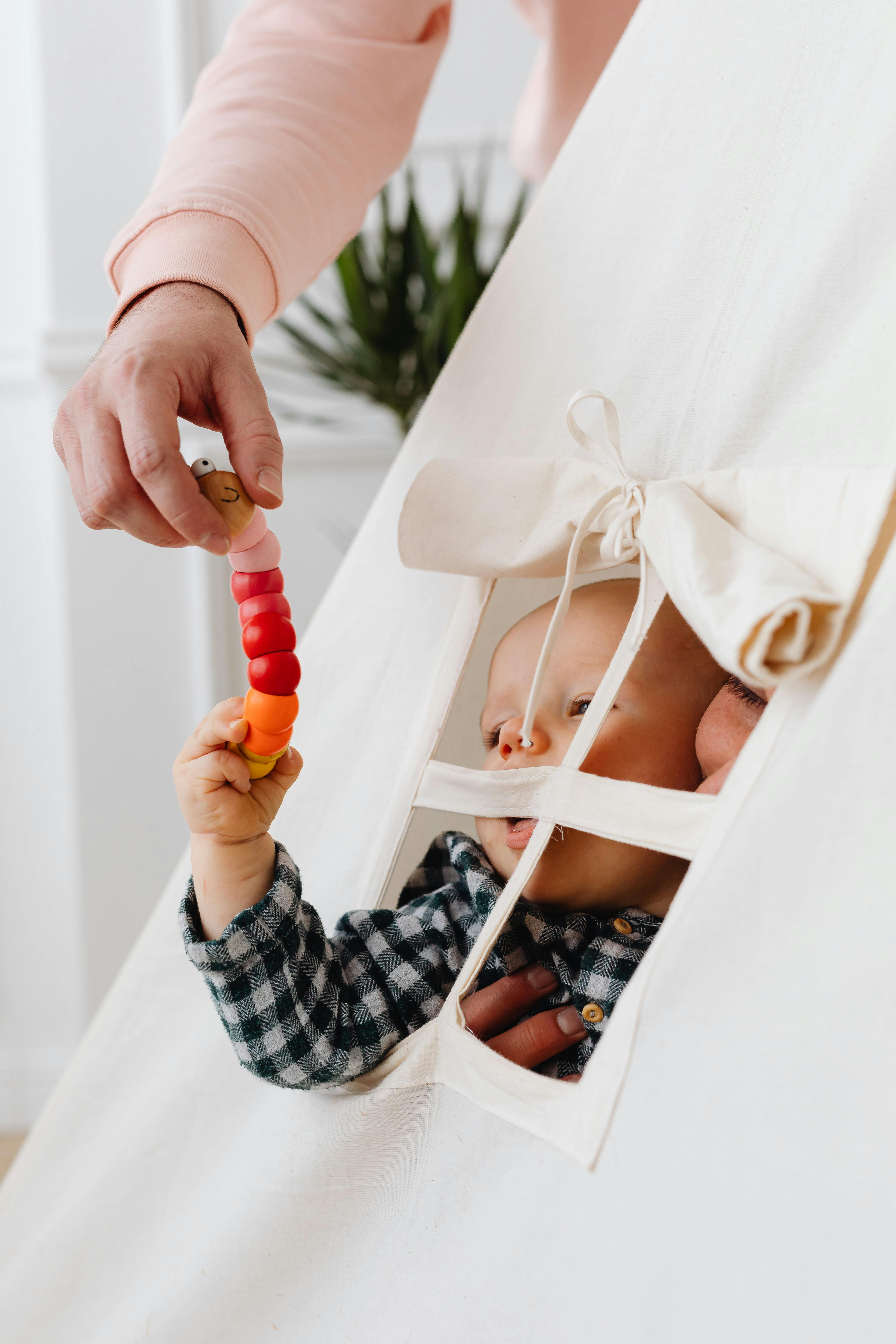 father giving a toy earthworm to a baby in a tent set up in the living room