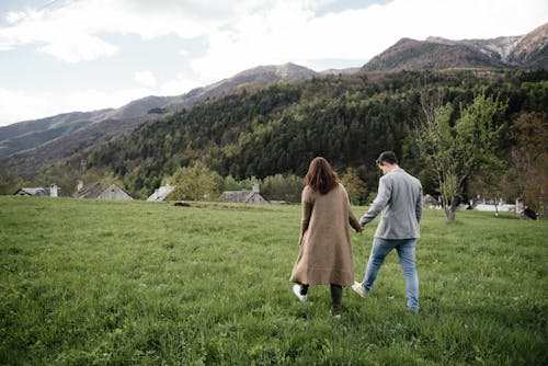 Man and Woman Holding Hands While Walking on Green Grass Field