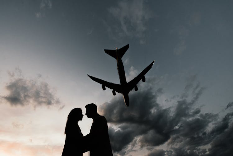 Silhouettes Of Couple Hugging Under Plane Flying In Sky