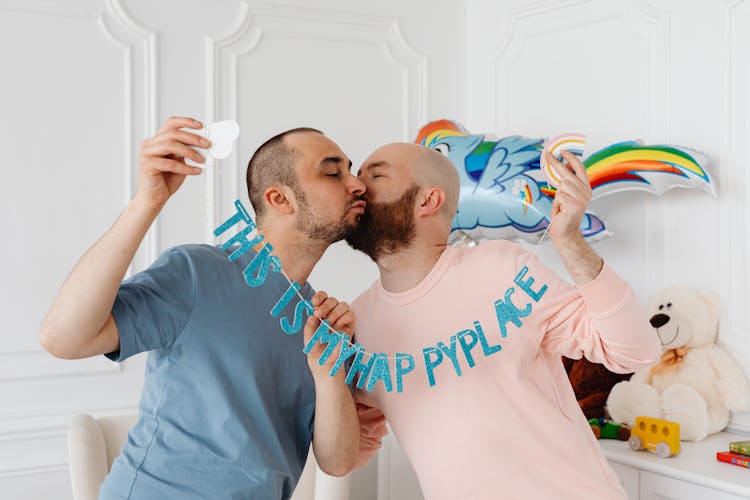 A Same Sex Couple Kissing While Holding Banner