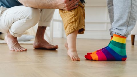 A toddler takes first steps with help from father indoors, showcasing love and support.