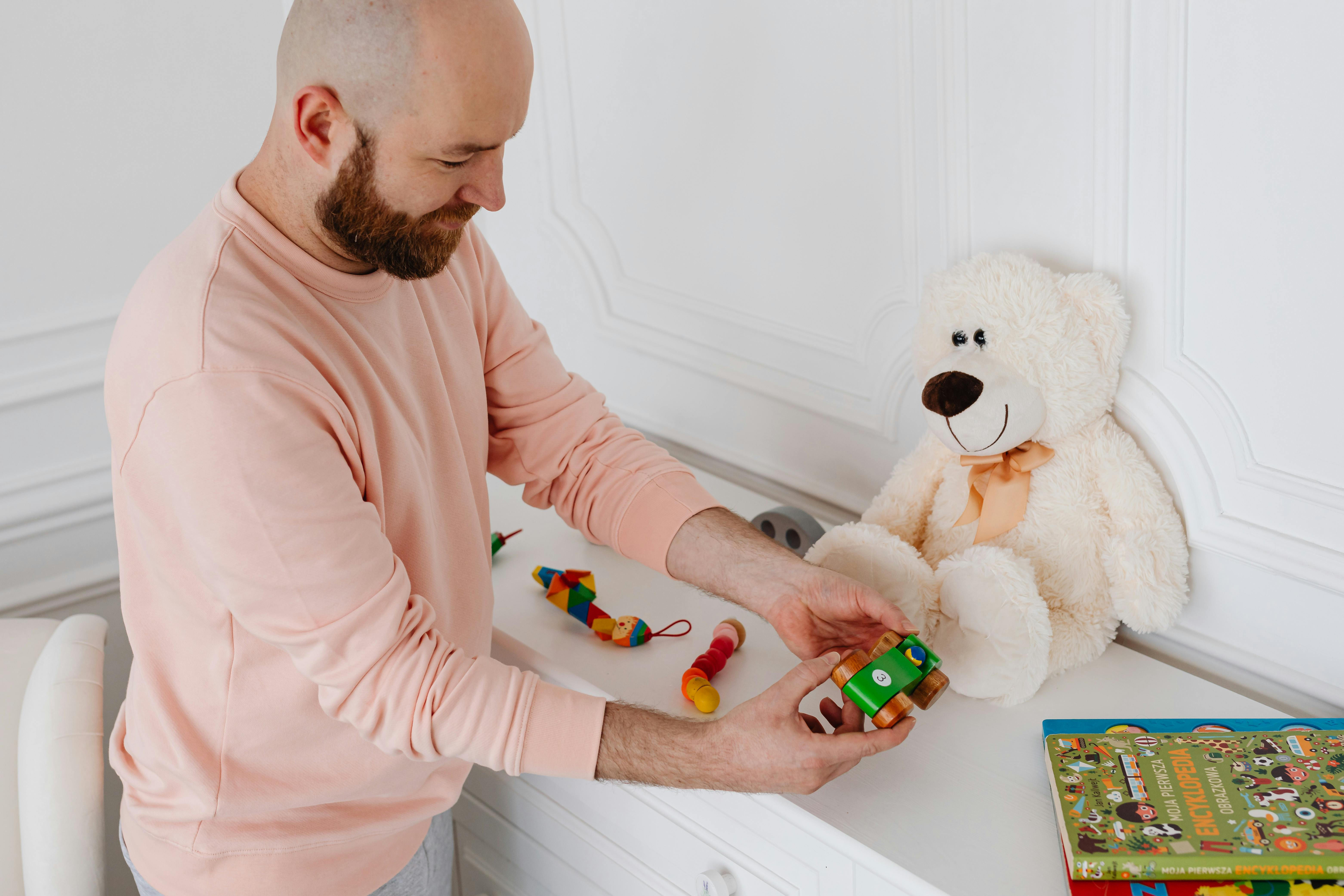 a bearded man in pink sweater holding a wooden toy