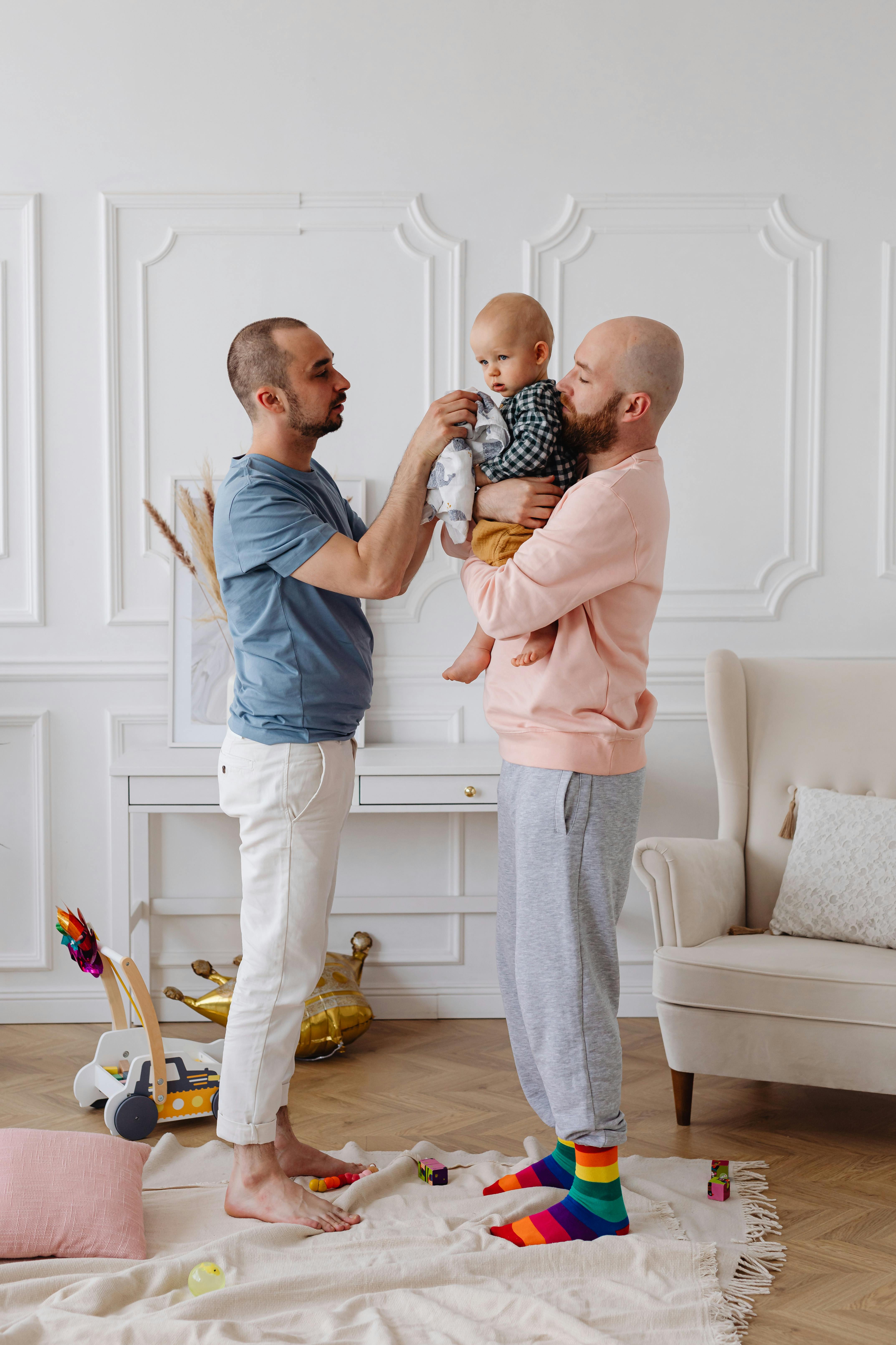 a same sex couple standing while taking care of their baby