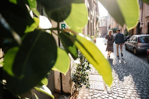 Free A couple holding hands walks along a charming cobblestone street with lush green foliage overhead. Stock Photo