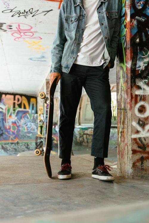 Free Skater leaning against a graffiti wall holding a skateboard at an urban skate park. Stock Photo