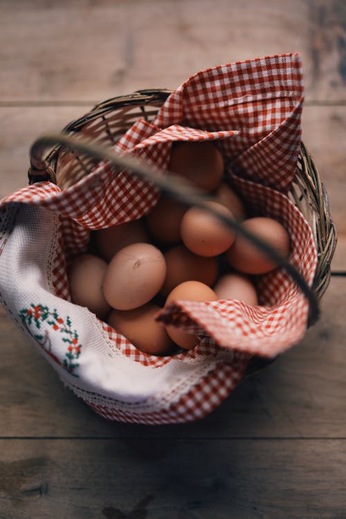 From above of wicker basket full of fresh chicken eggs placed on wooden table in daytime