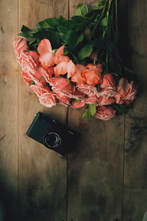 Bouquet of flowers and retro photo camera placed on wooden table