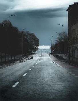 Moody street scene in Gdynia, Poland, showcasing an empty road leading towards the sea under a stormy sky.