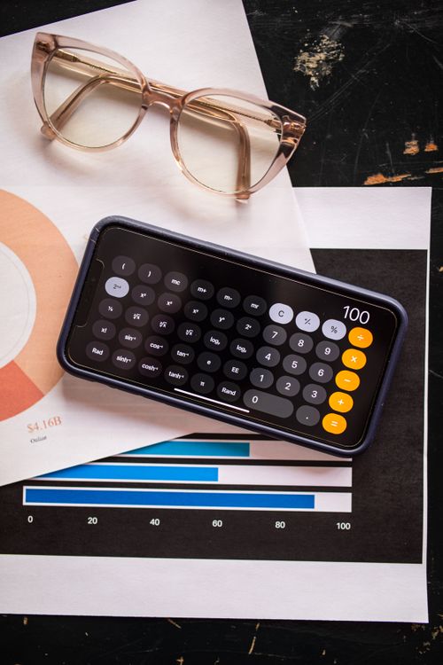 Free A smartphone with calculator app on a financial report with eyeglasses, depicting data analysis. Stock Photo