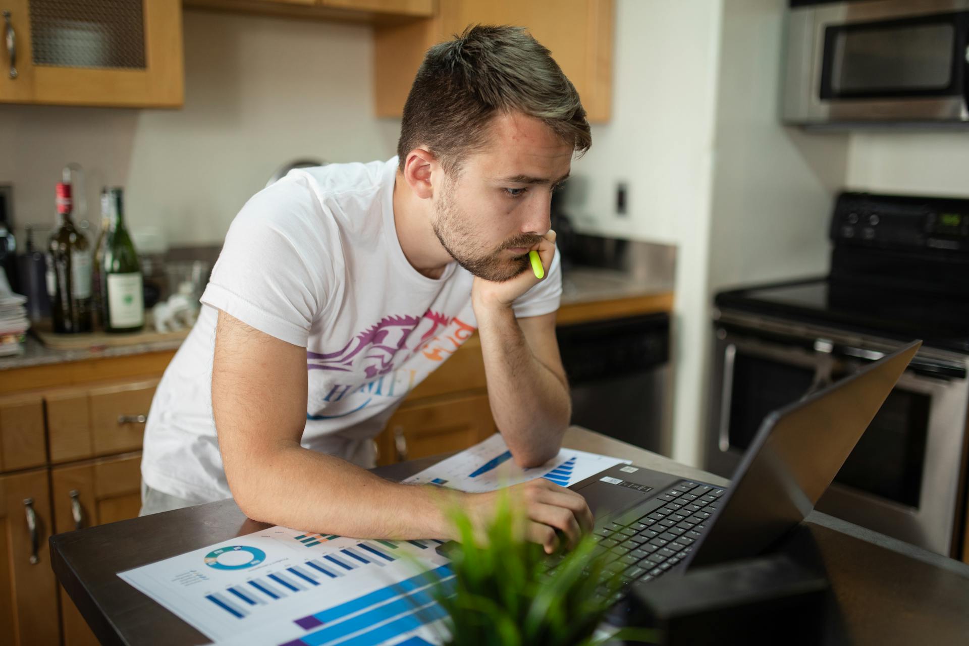 Young man concentrating on data analysis at home, working with laptop and charts.