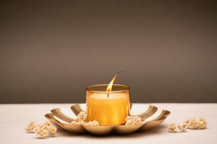 A Lighted Candle On Container With Flowers