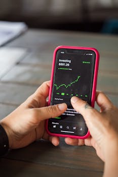 Close-up of hands holding a smartphone with stock market data on the screen.