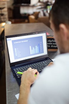 Man reviewing company revenue charts on a laptop indoors, showcasing data analysis and finance work.