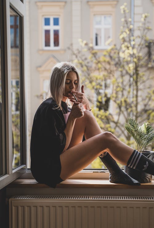 Free A Woman in Black Shirt Sitting by the Window while Smoking Weed Stock Photo