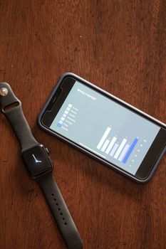 Smartphone and smartwatch displaying data on a wooden table, highlighting technology and analytics.
