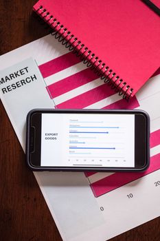 Top view of market research documents and smartphone showing export data charts.
