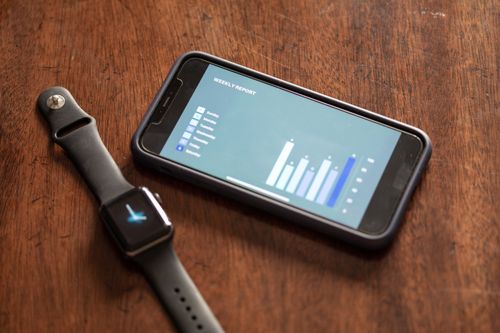 Free Smartphone displaying weekly report chart alongside a smartwatch on a wooden surface. Stock Photo