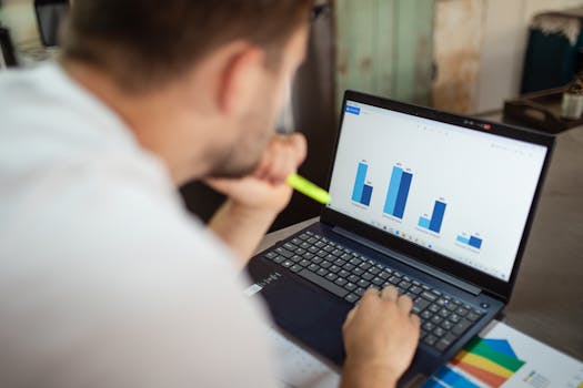 Man reviewing business charts on a laptop from an over-the-shoulder angle.