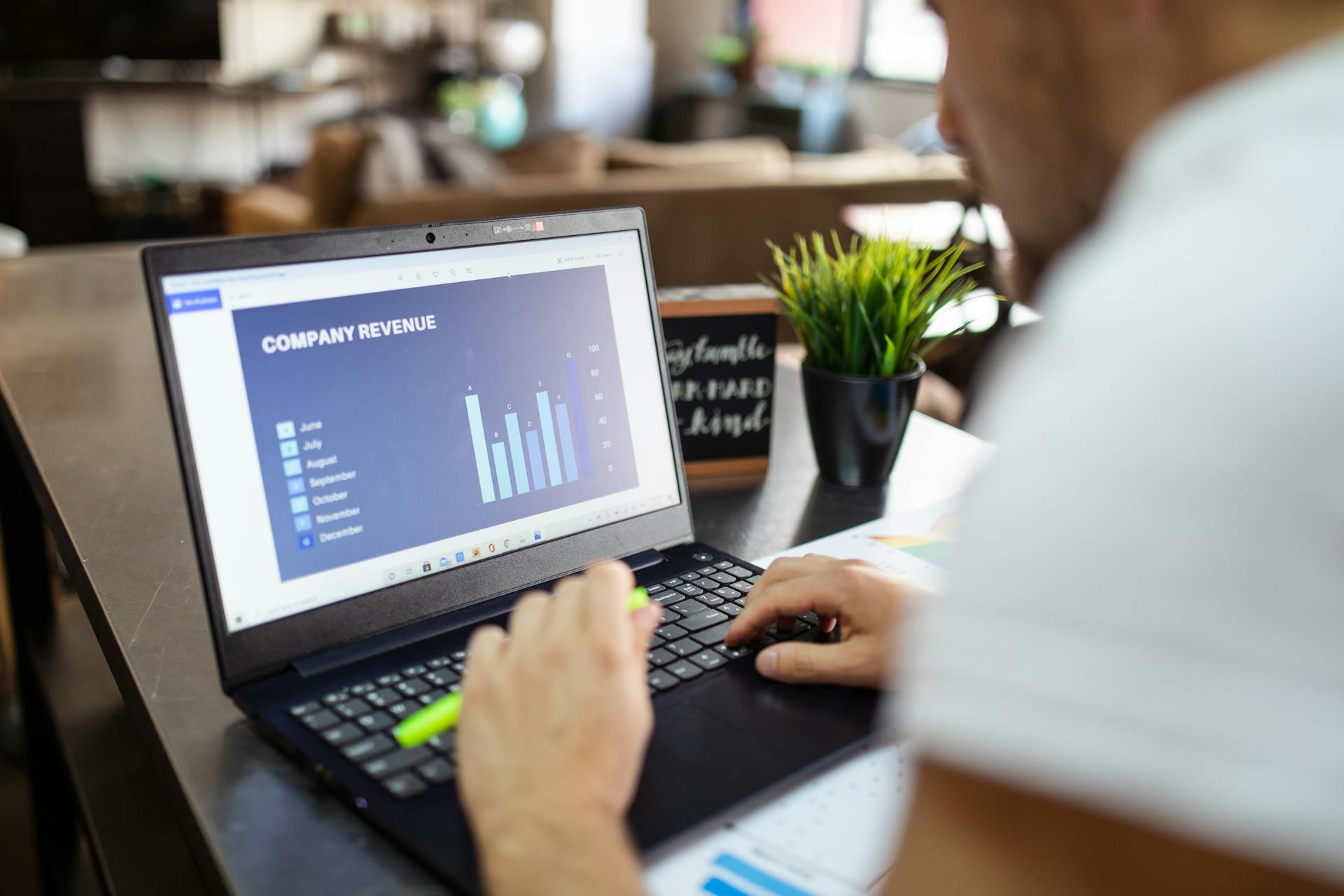 Man using a laptop to analyze company revenue data with graph charts in office setting.