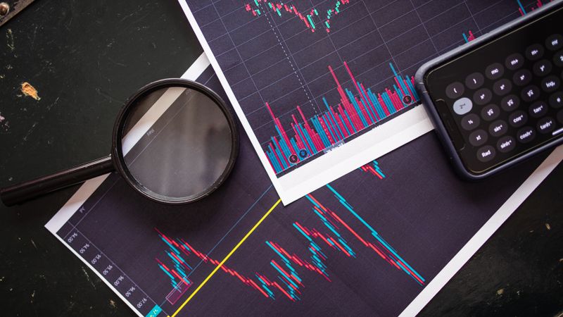 Stock market charts analyzed with a magnifying glass and calculator for financial research.