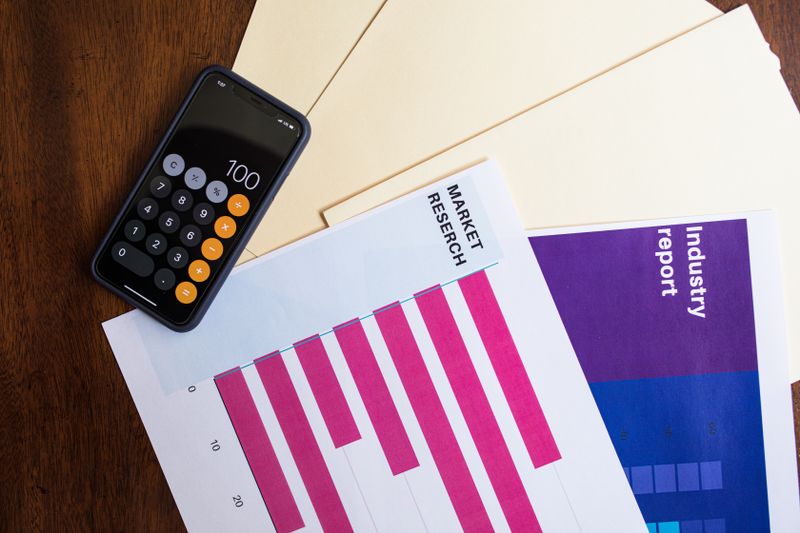 Flat lay of smartphone and market research papers on wooden table for business analysis.