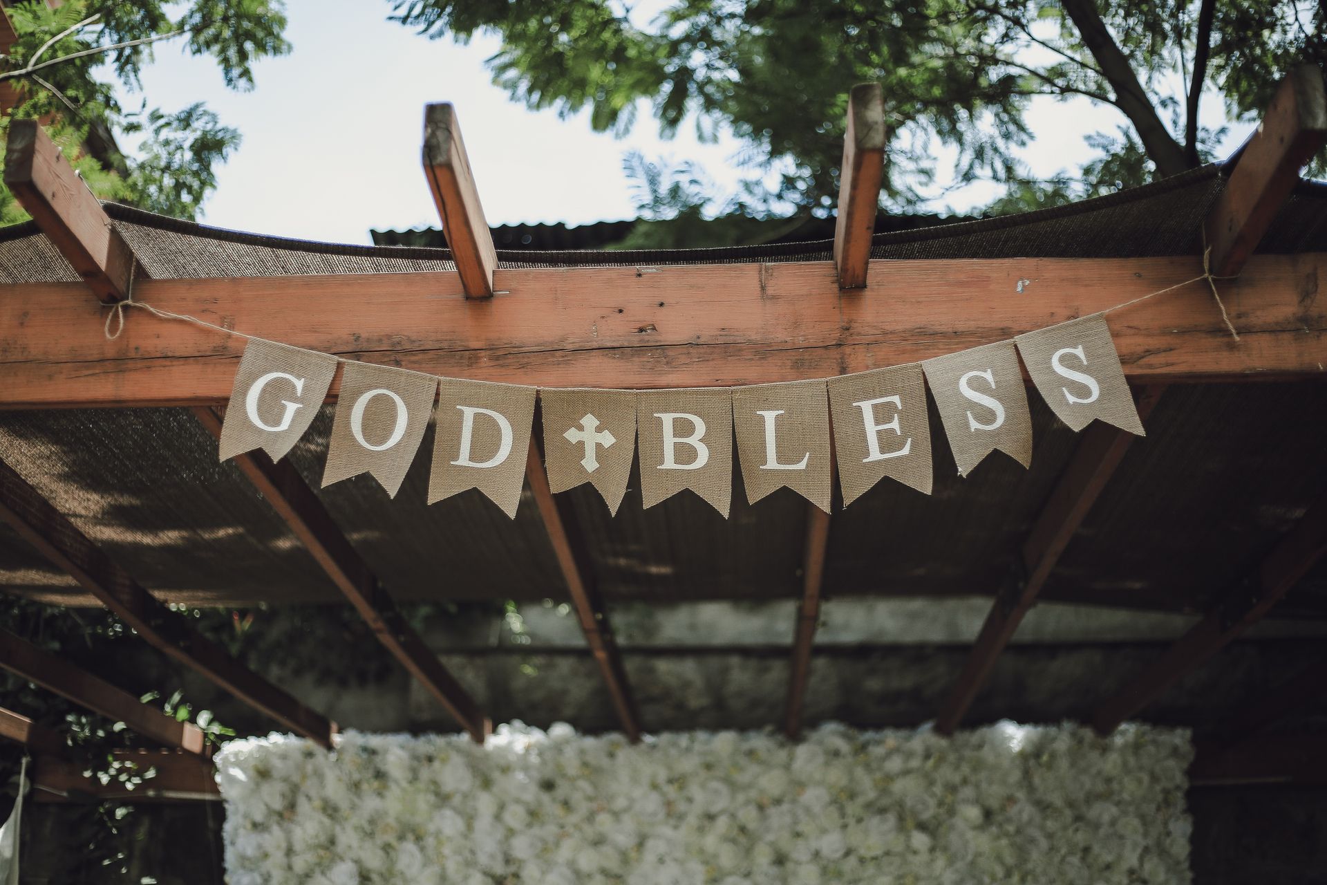 A charming pergola adorned with a 'God Bless' banner, set in a lush, outdoor environment.