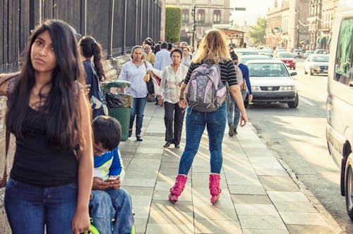Женщина в черной футболке, голубых джинсах и розовых роликовых коньках катается на улице