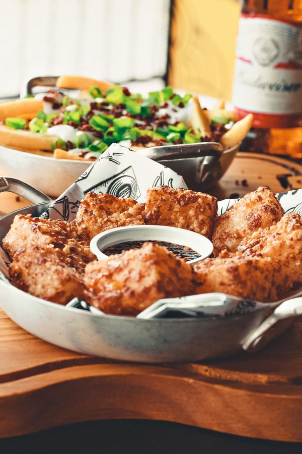 Aperitivos fritos crocantes servidos com um molho para mergulhar em uma bandeja de madeira rústica.