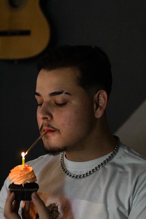 Man in White Crew Neck Shirt Lighting a Cigarette on Cupcakes With Lighted Candle