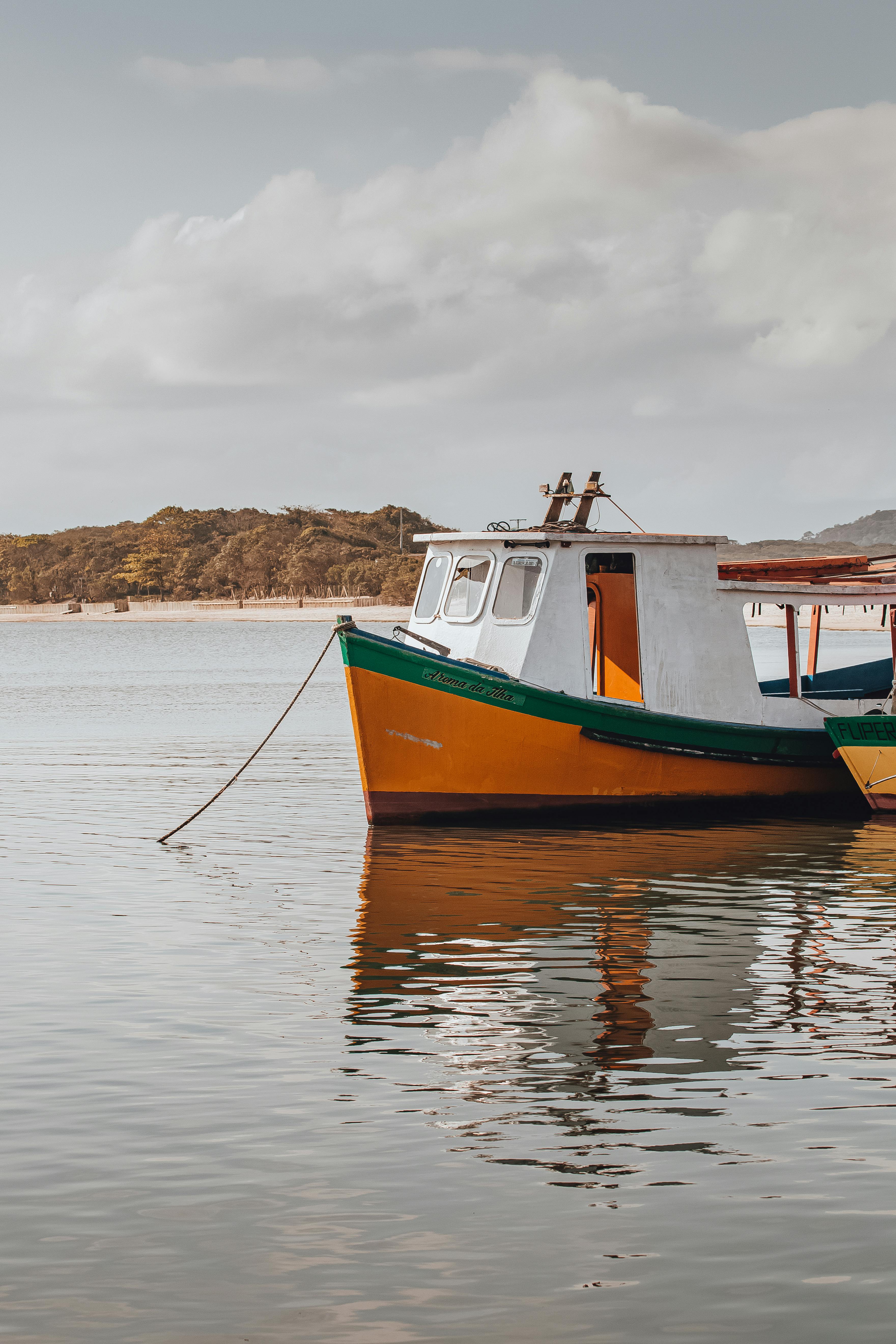 A vibrant yellow and green fishing boat moored on calm waters near lush Brazilian coastline.