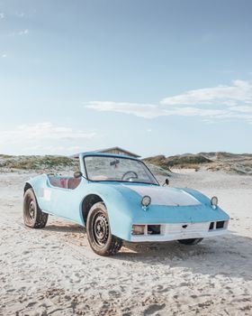 A classic blue car parked on a sandy beach under a clear sky in Brazil.