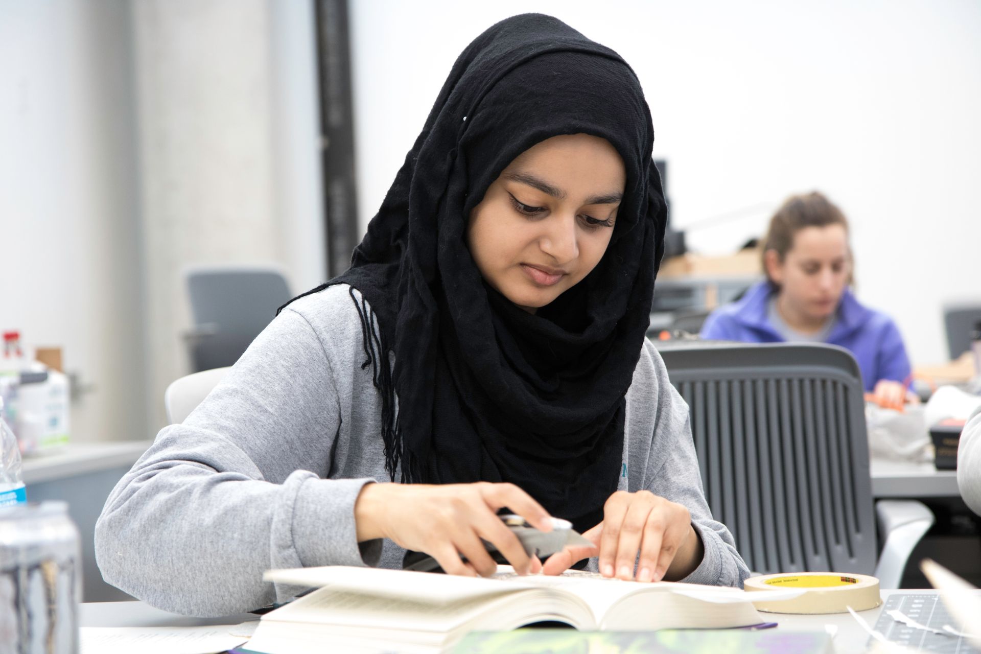 A young woman in a hijab studies intently at a college classroom, representing education and diversity.