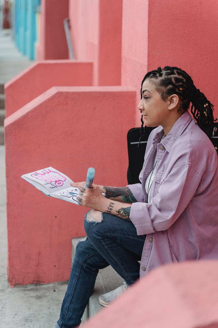 Ethnic Woman Sitting Outside And Drawing In Sketchbook