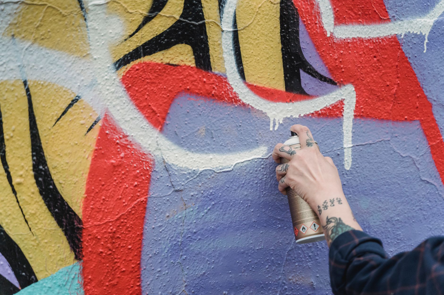 A tattooed individual sprays paint from a can