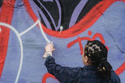 Free Back view of unrecognizable female artist with black braided hair spraying white paint on colorful wall while standing on street Stock Photo