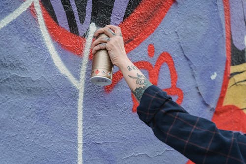 Close-Up Photo of a Person's Hand Spraying White Paint on a Wall