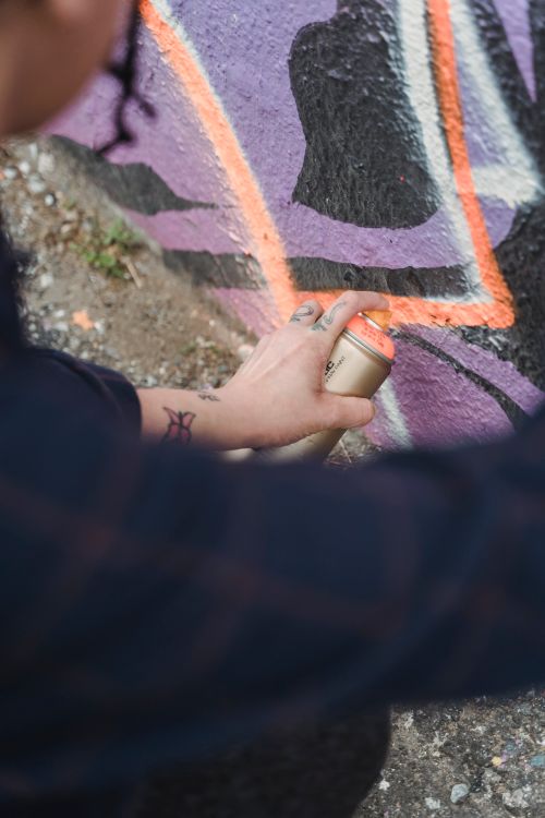 Free Crop anonymous painter in black wear spraying colorful paint from spray can on wall with creative patterns on street of city Stock Photo