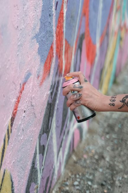 Close-up of a tattooed hand spray painting colorful graffiti on a wall.