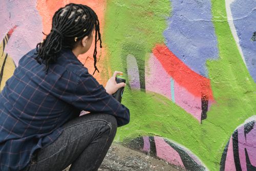 Free Side view of anonymous skilled female artist in casual wear hunkering down near colorful wall while painting graffiti on street Stock Photo