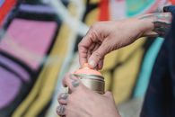Soft focus of crop unrecognizable painter with tattoos opening spray paint can while standing near colorful wall with creative graffiti