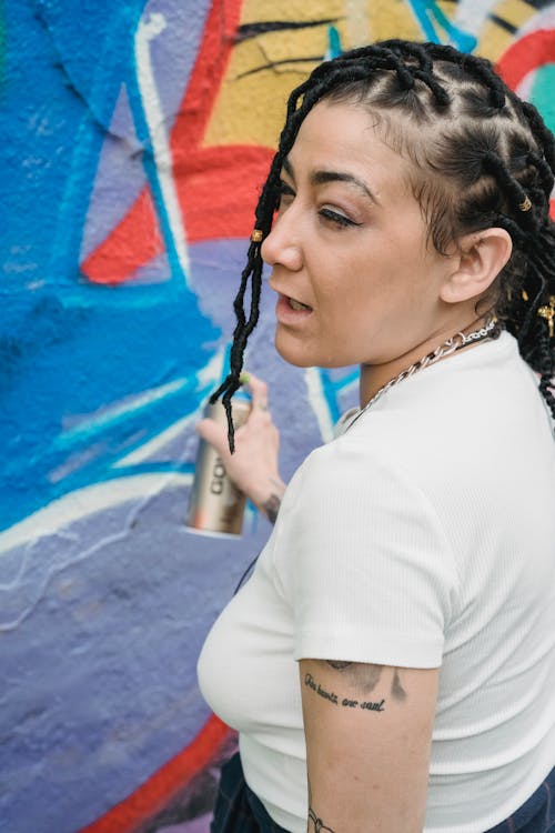 Woman in a White Shirt Holding a Spray Paint Near a Wall with Graffiti