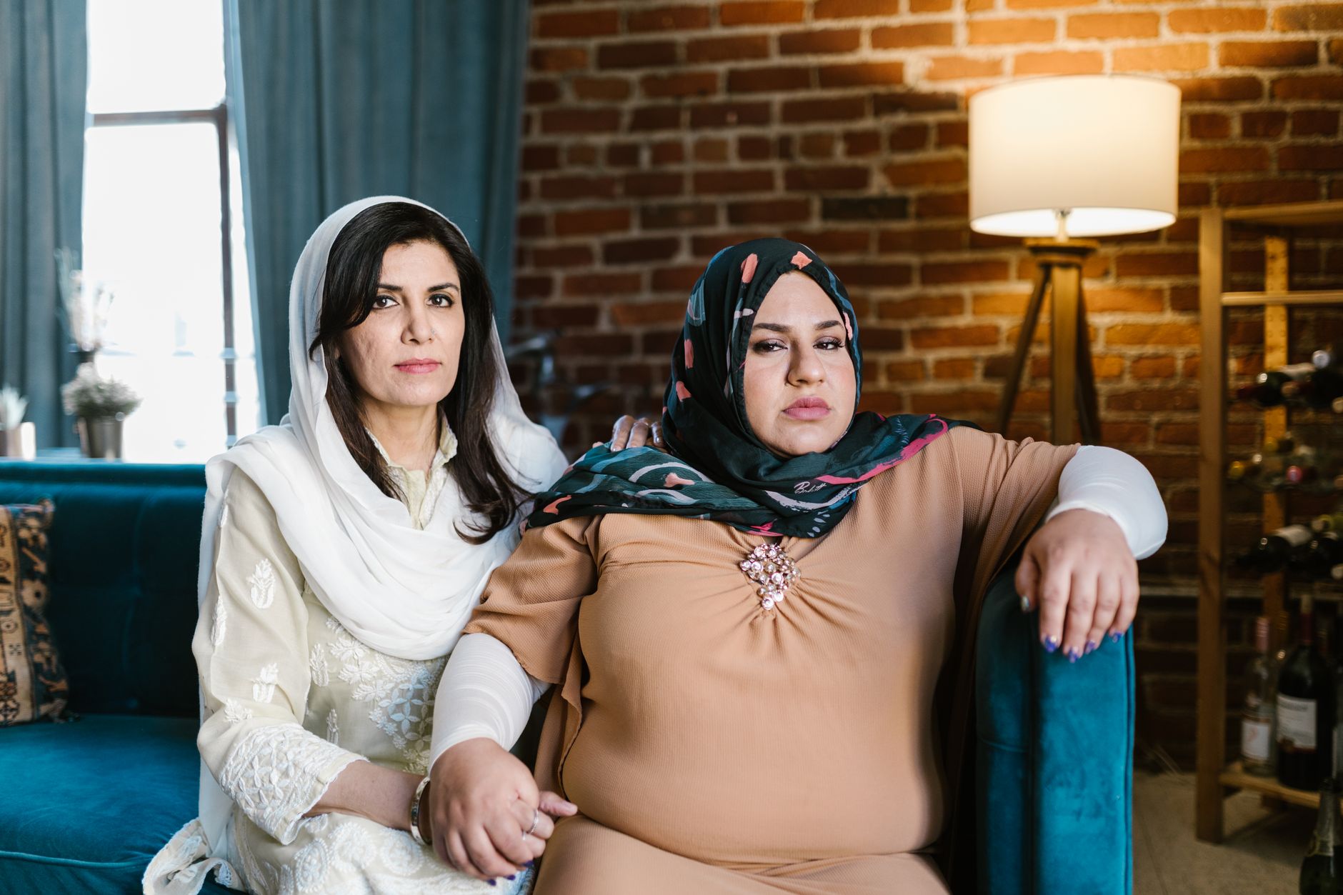 Two women in hijabs sitting closely on a blue sofa, showcasing togetherness and warmth.