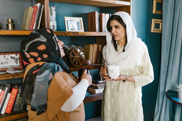 Two Women In Hijabs Holding Cups Of Coffee And Talking 