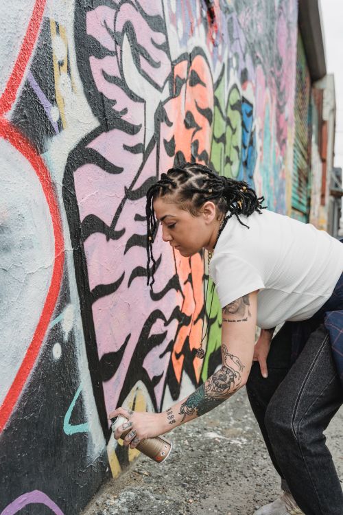 Free A female street artist spray paints vibrant graffiti on a wall outdoors. Stock Photo