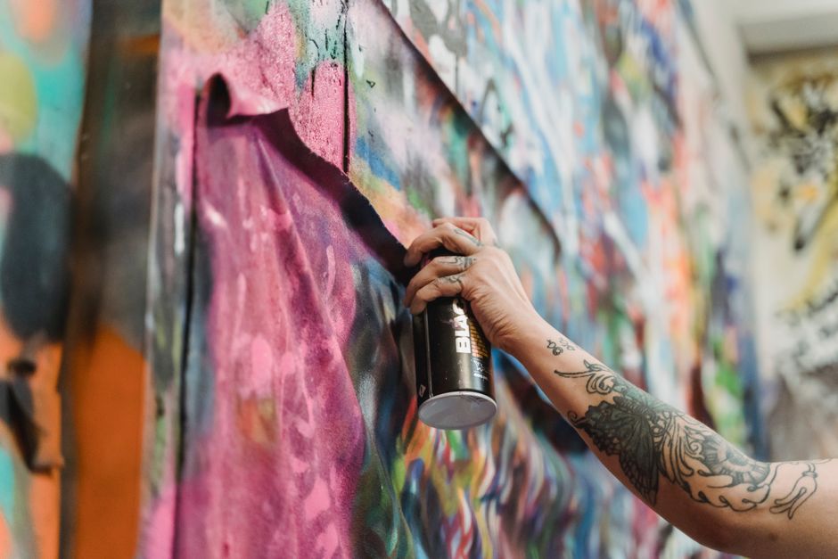 Close-up of tattooed hand spray painting a colorful graffiti wall. Vibrant urban art scene.