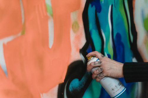 Free A detailed view of a tattooed hand using spray paint to create vibrant graffiti on a wall. Stock Photo