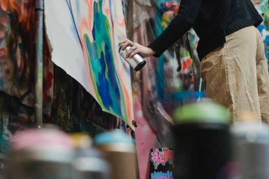 Artist using spray paint to create vibrant graffiti on canvas indoors.