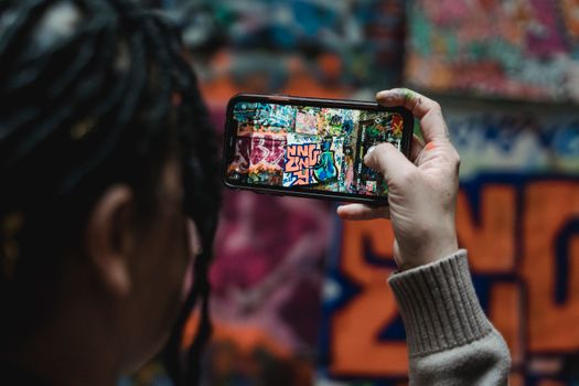 A person photographs colorful graffiti art using a smartphone, showcasing urban creativity.