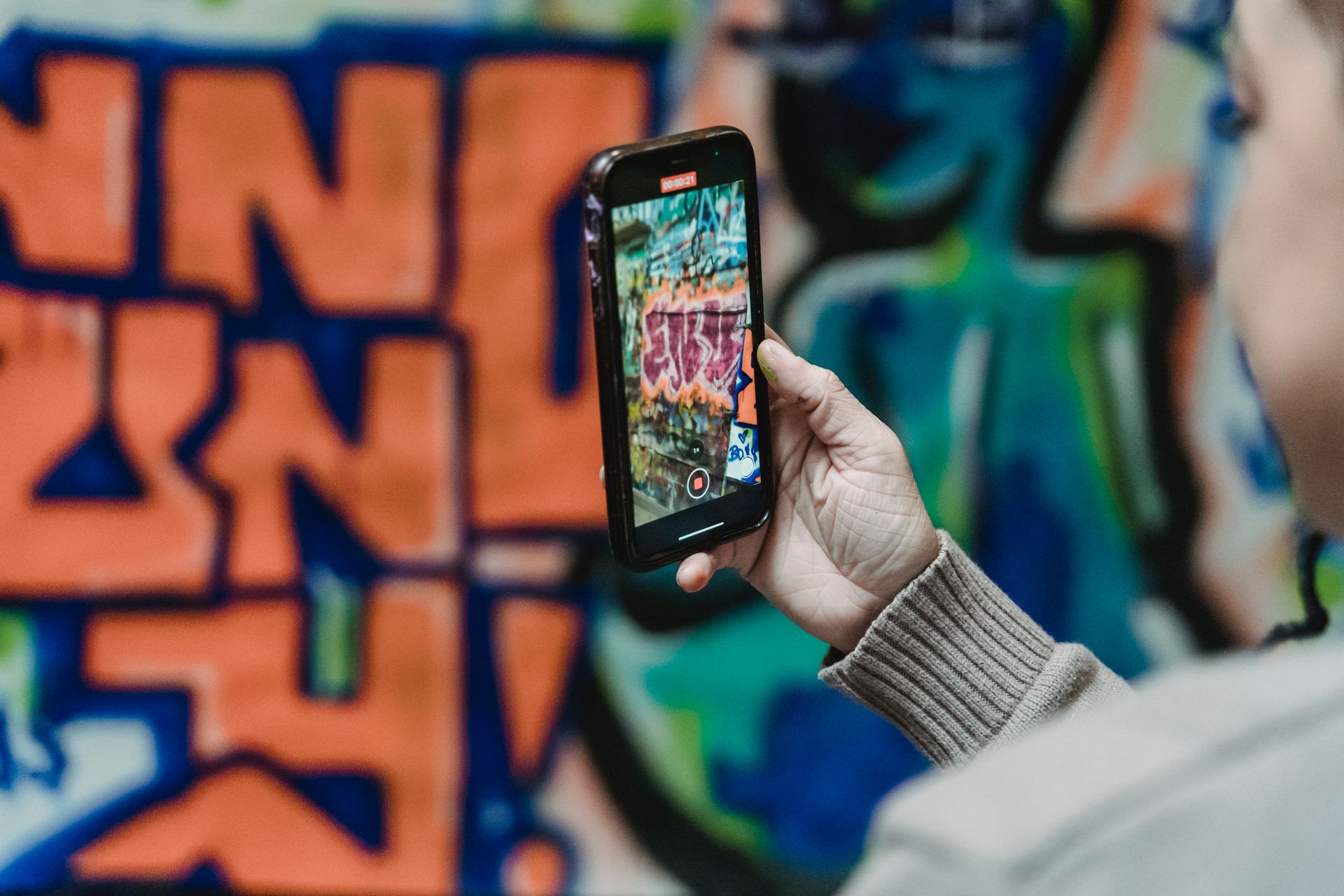 Person using smartphone to photograph colorful graffiti wall with artistic design.