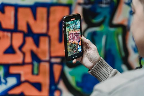 Free Person using smartphone to photograph colorful graffiti wall with artistic design. Stock Photo